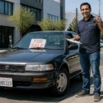 Mężczyzna stoi obok czarnej Toyoty z tablicą For Sale przed biurowcem.